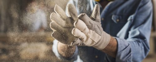 Unrecognizable male hands with work gloves on, clapping to remove sawdust
