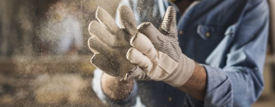 Unrecognizable male hands with work gloves on, clapping to remove sawdust